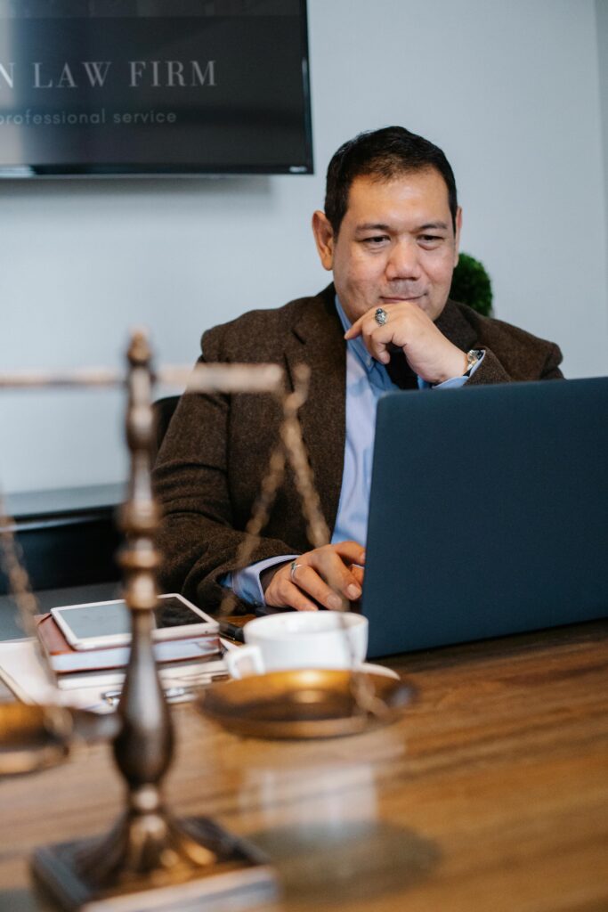 pexels-photo-5673484-5673484 Cheerful ethnic legislator in formal outfit working with netbook at table with scales of justice and tablet